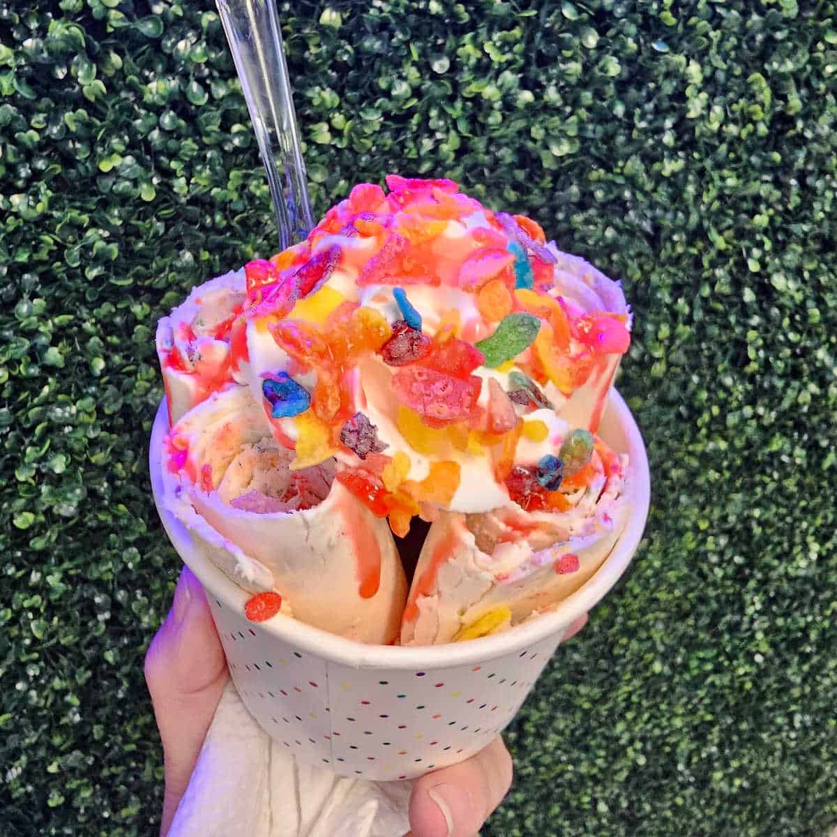 hand holding a bowl with fruity pebbles topped rolled ice cream