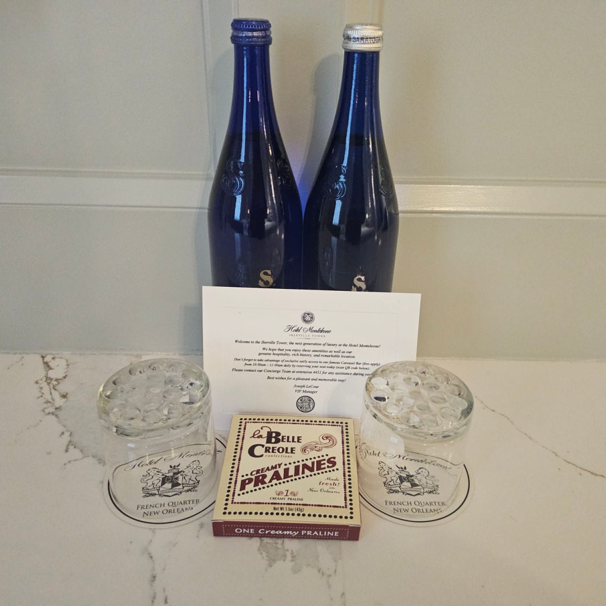 two blue glass bottles behind two glasses and a package of belle creole creamy pralines