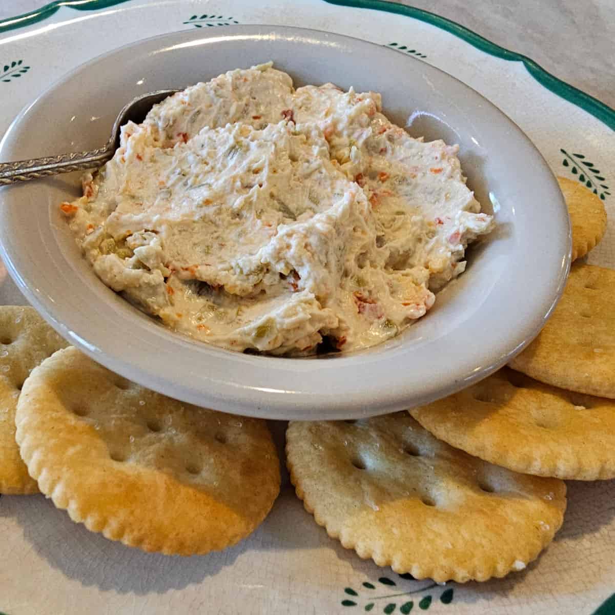 Olive pimento cheese in a white bowl with a plate of ritz crackers
