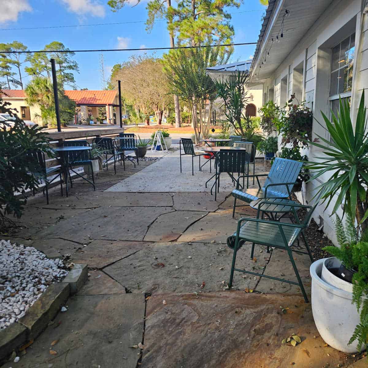 Outdoor seating with green chairs and metal tables outside of Isla Wine with tropical plants