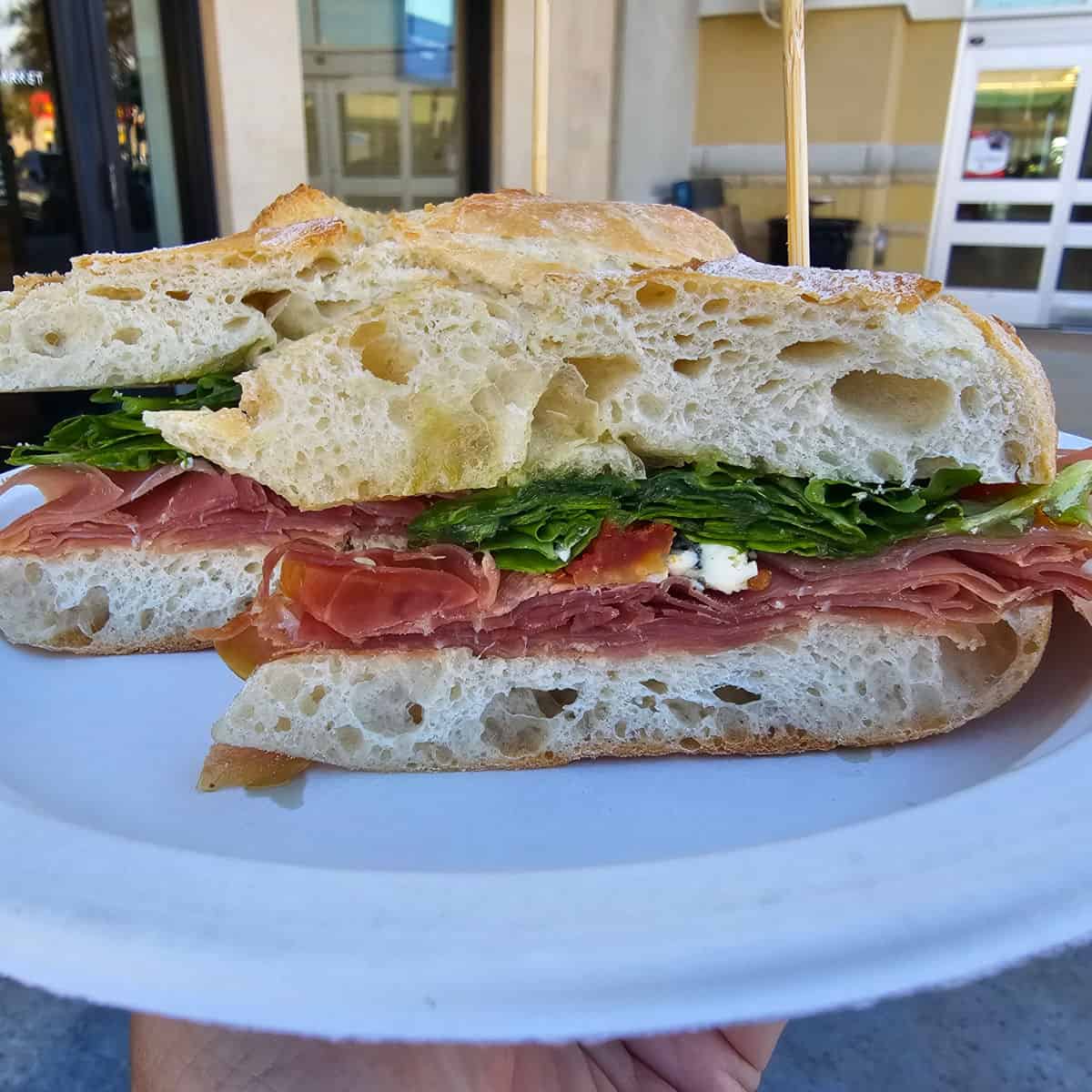 Hand holding a paper plate with a Prosciutto Sandwich