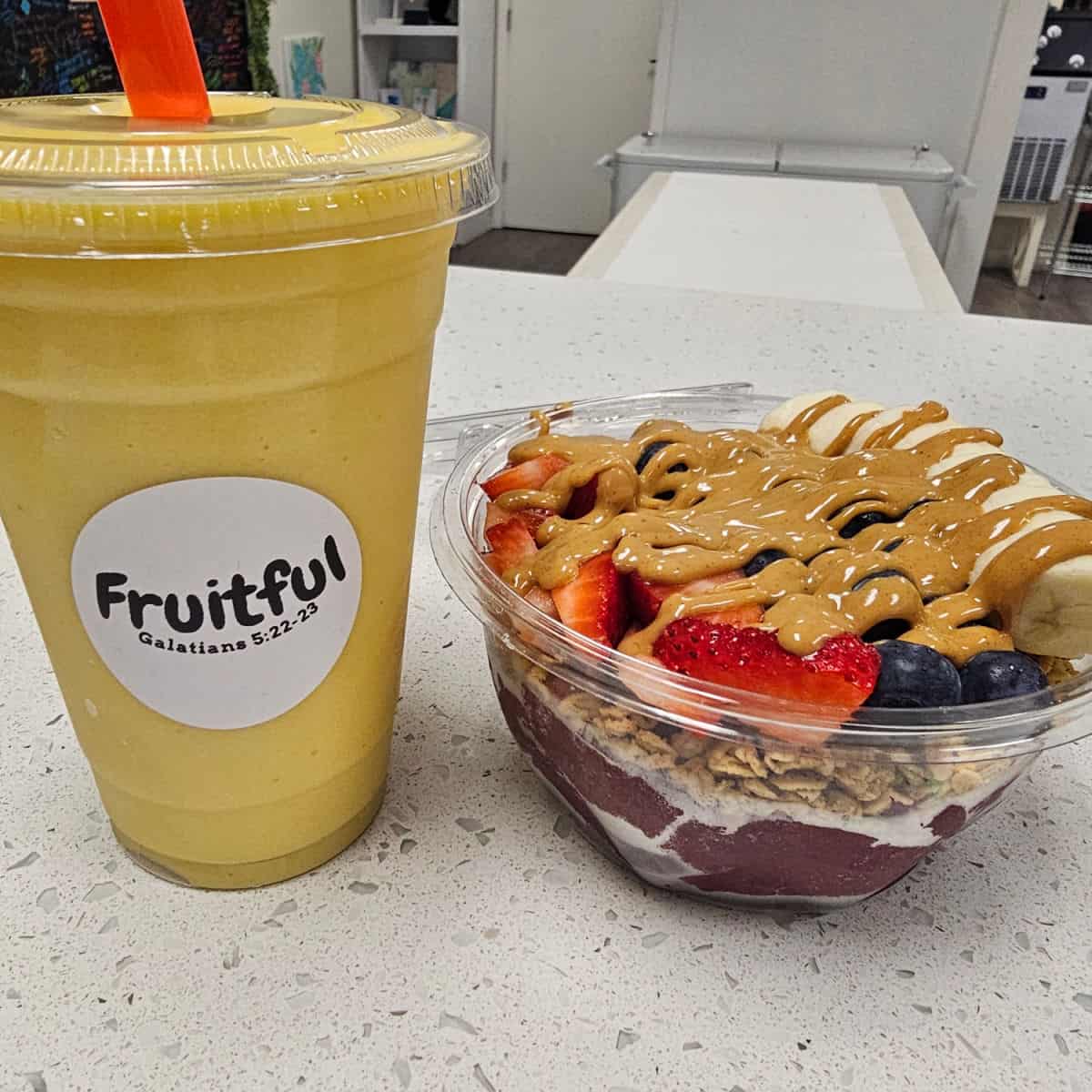 Mango smoothie next to an acai bowl with fruitful sticker on the smoothie