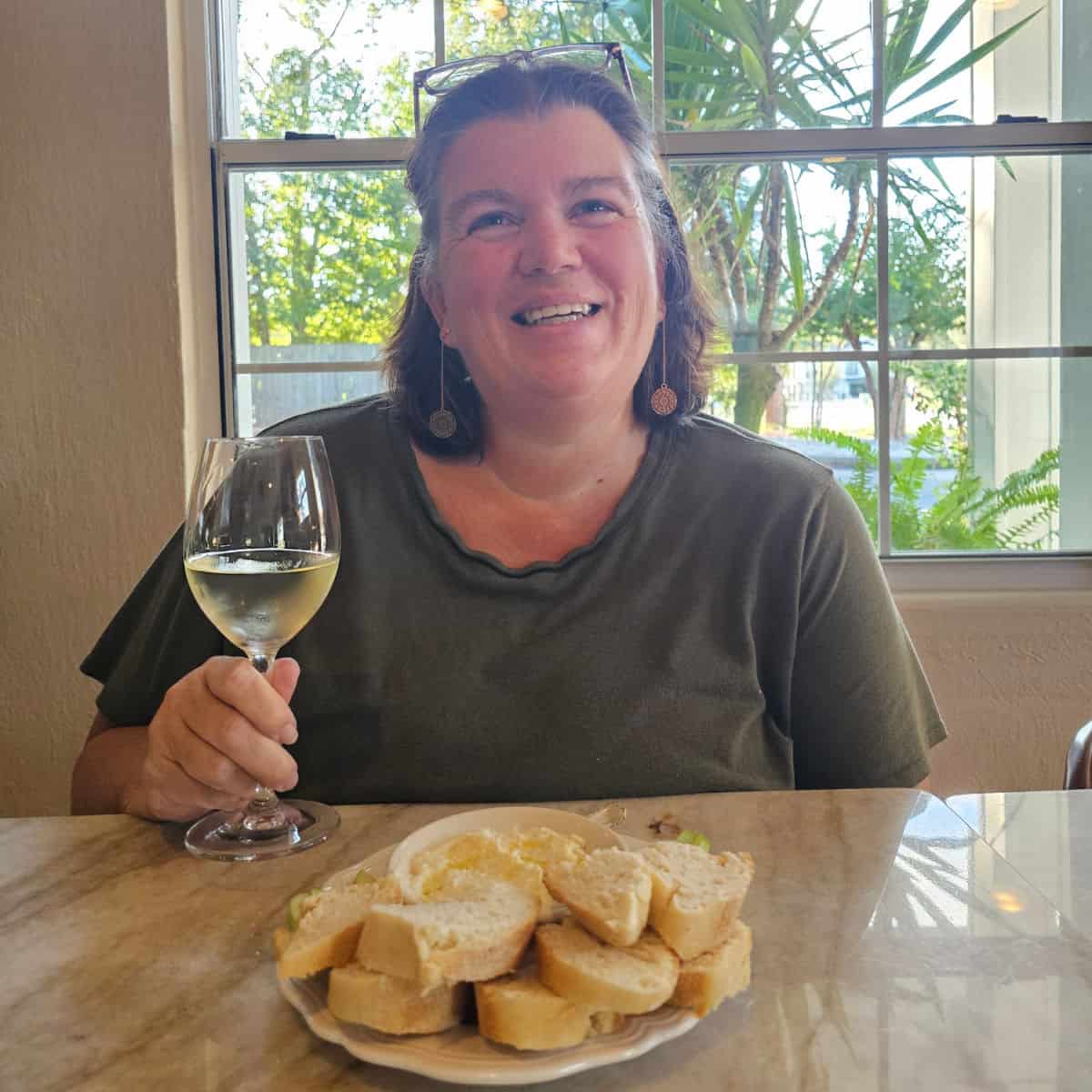 Tammilee holding a glass of wine with a plate of whipped ricotta dip and bread