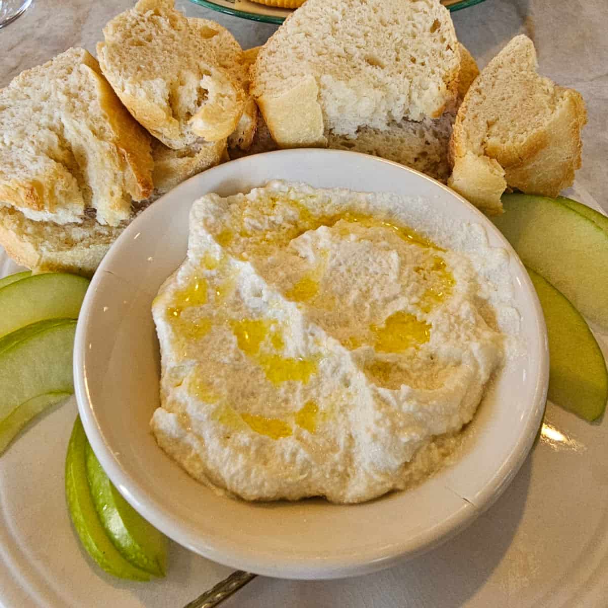 Whipped ricotta in a white bowl and bread and apples on a plate
