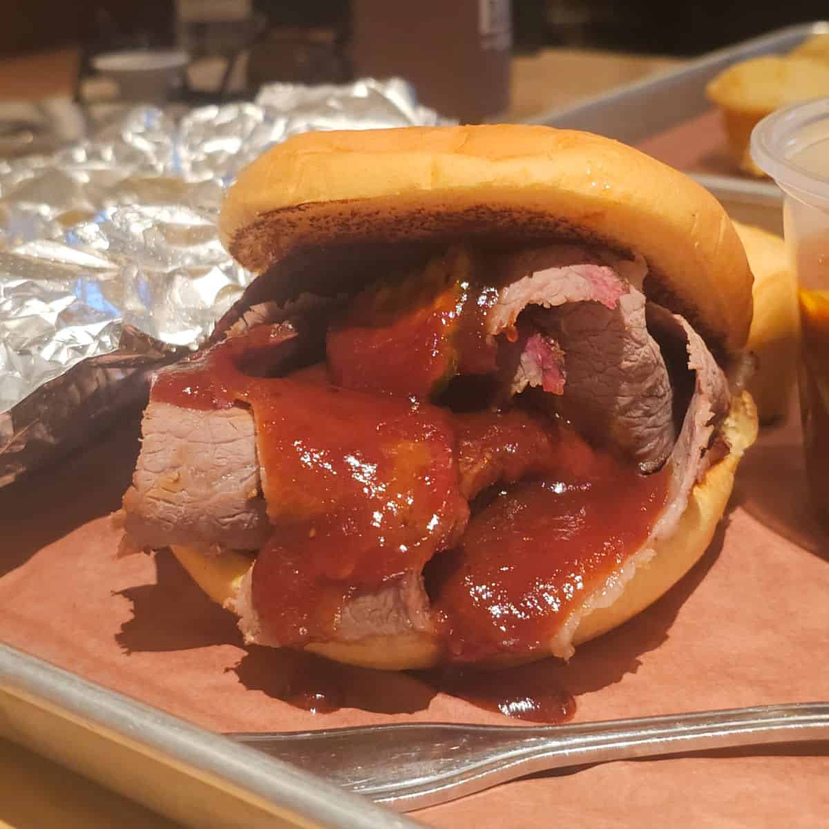 beef brisket sandwich with sauce on a bun sitting on a tray at Jim n Nicks BBQ