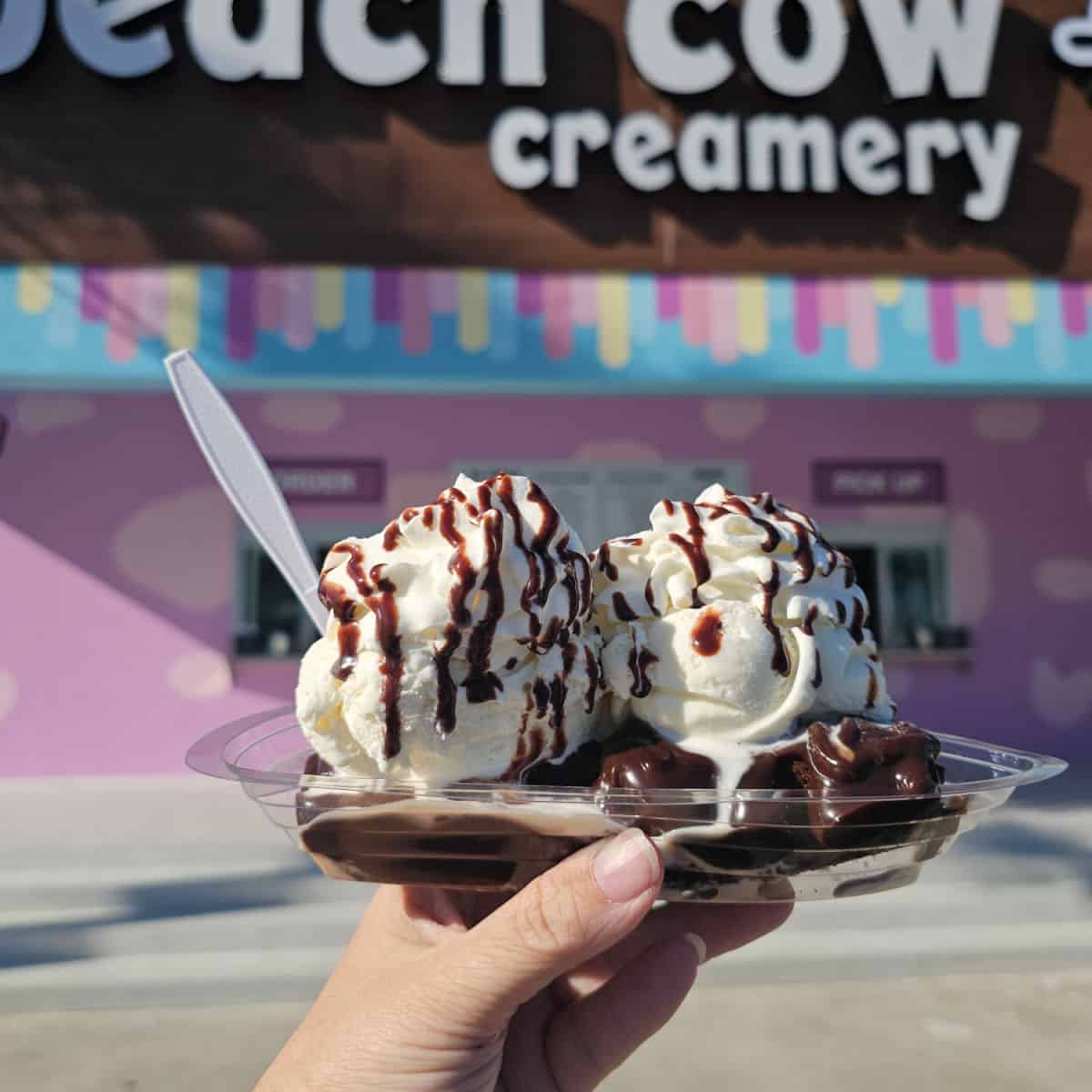 Hand holding a brownie sundae in front of Beach Cow Creamery