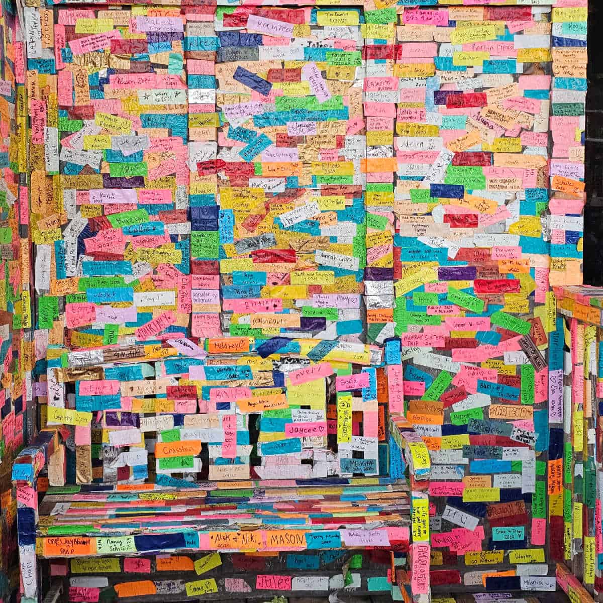 Wall covered in colorful pieces of duct tape with names an sayings on them