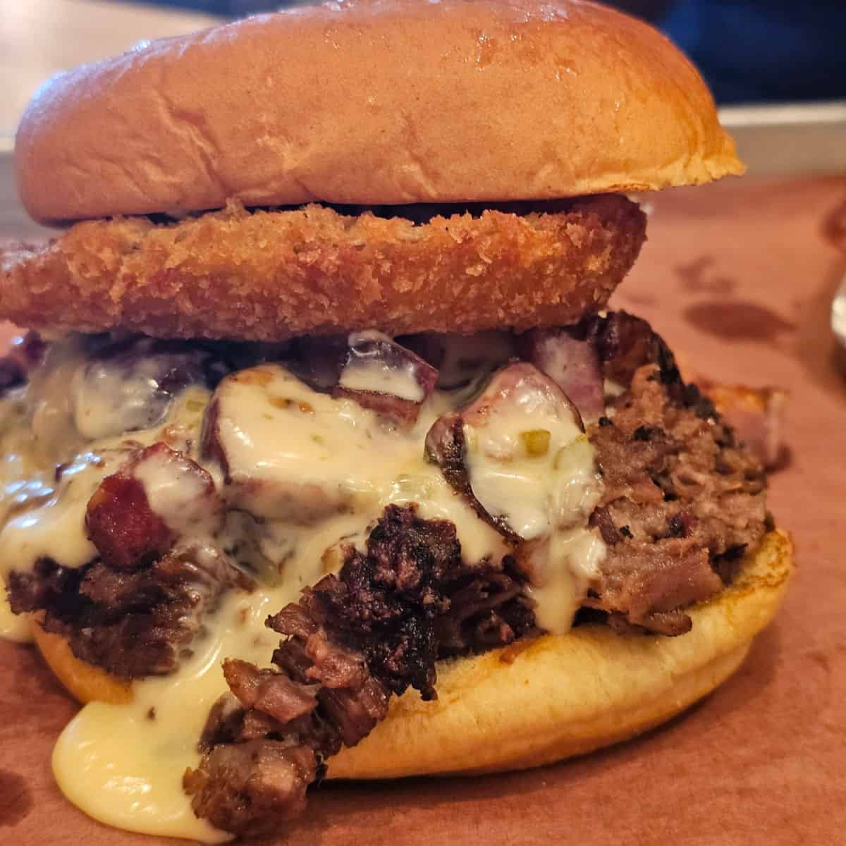sandwich with queso and an onion ring on a silver tray
