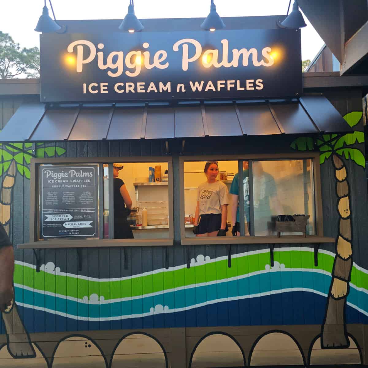 Piggy Palms Ice Cream n Waffles sign over a building with two palm trees and a blue and green wave on it