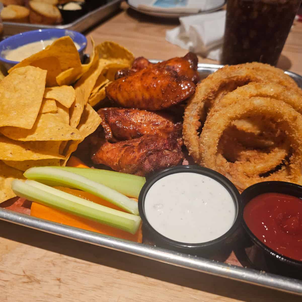 Southern trio appetizer at Jim n Nicks on a silver tray with chips and queso, wings, and onion rings plus sauces