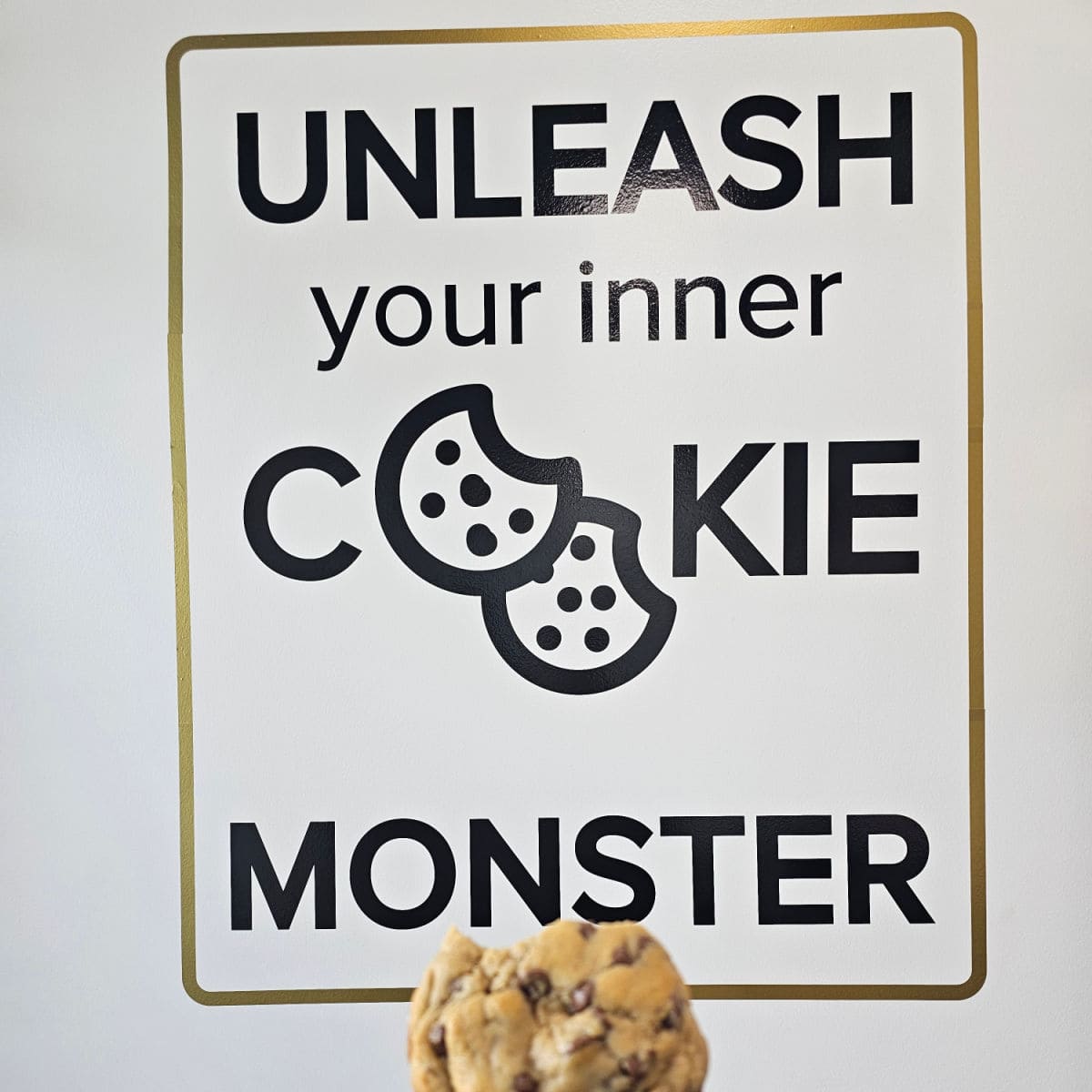 Unleash your inner cookie monster sign with a hand holding a chocolate chip cookie