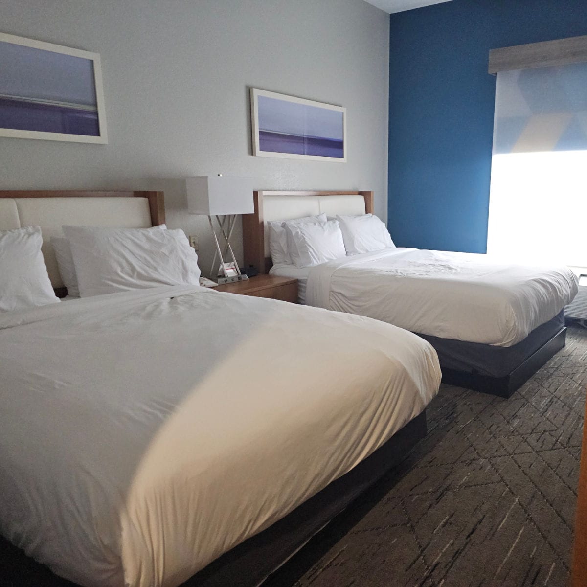 2 queen beds with white linens, table and lamp in between them