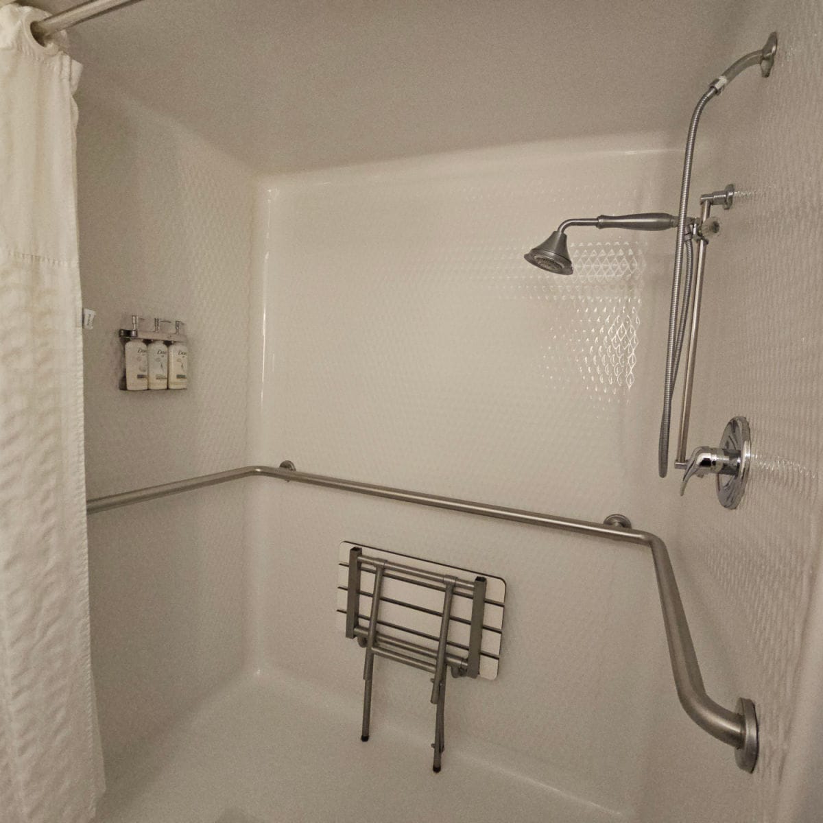 accessible shower with a fold down bench, shower head, and shampoo conditioner and body soap on the wall