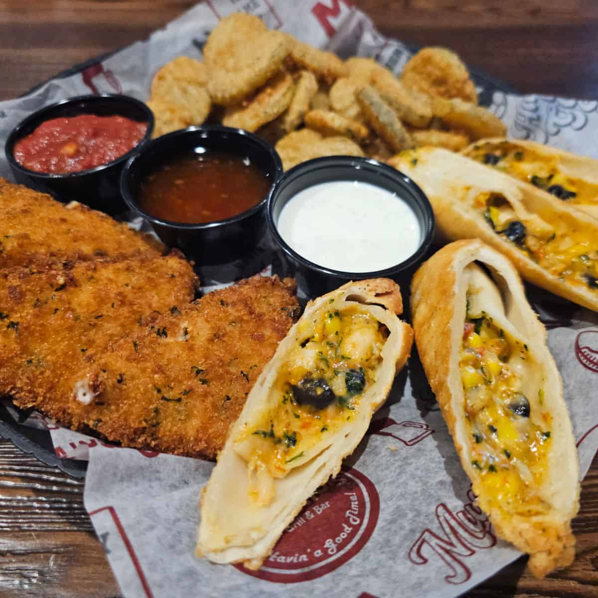 Appetizer combo platter with egg rolls, mozzarella wedges, and fried pickles with three sauce cups