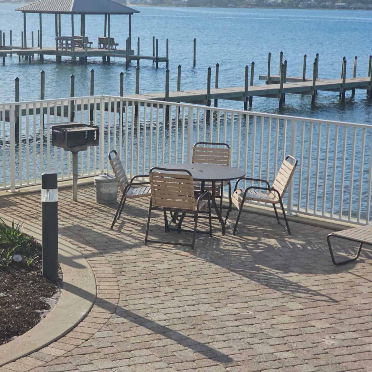 table with four chairs next to an outdoor barbecue, fence around the area and Little Lagoon in the background