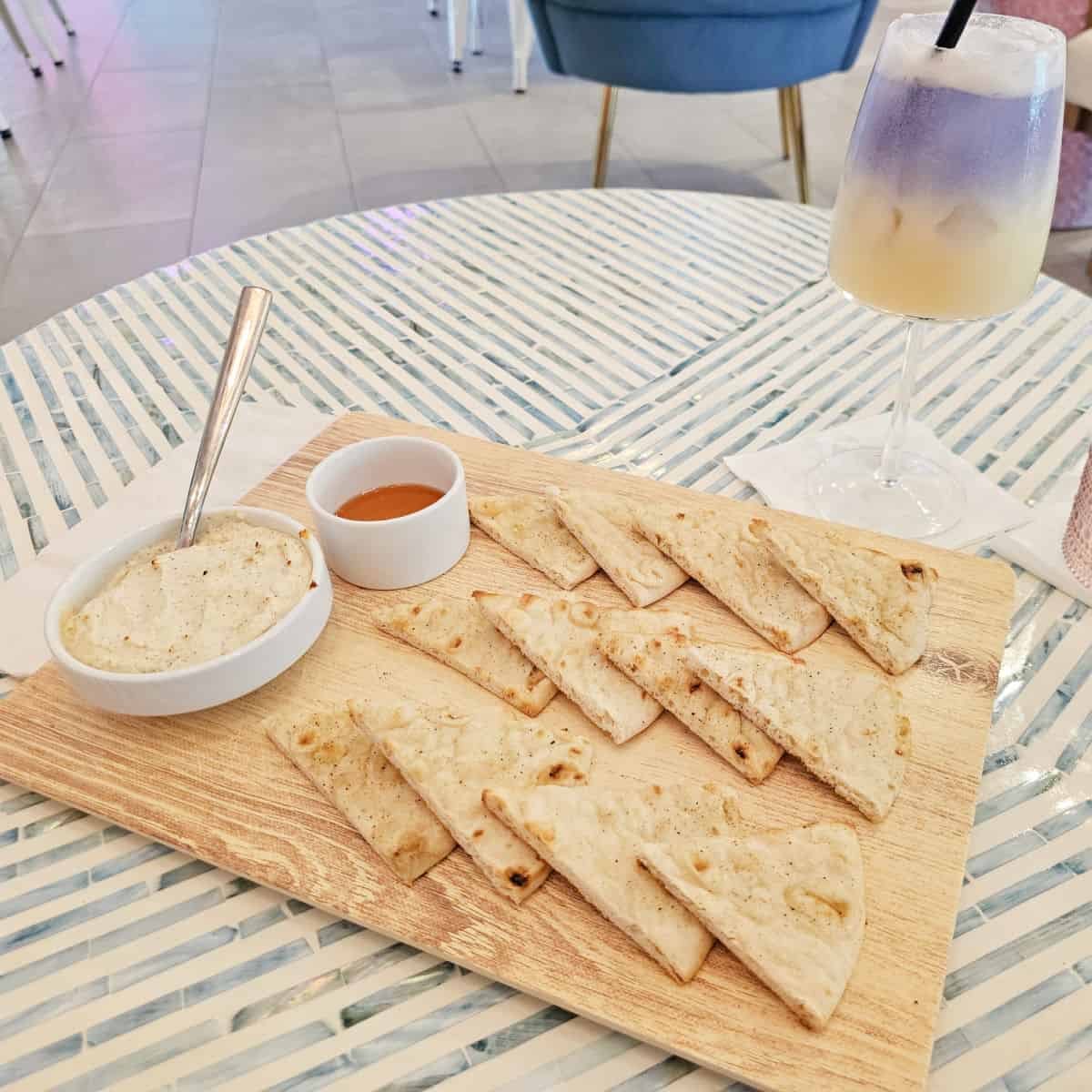 Platter with baked feta dip and bread points, next to a cocktail sitting on a round table