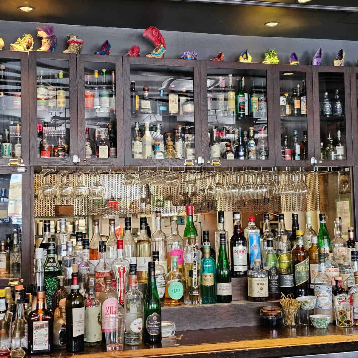Compere Lapin Bar area with bottles on shelves, glasses hanging and mardi gras high heels across the top of the bar