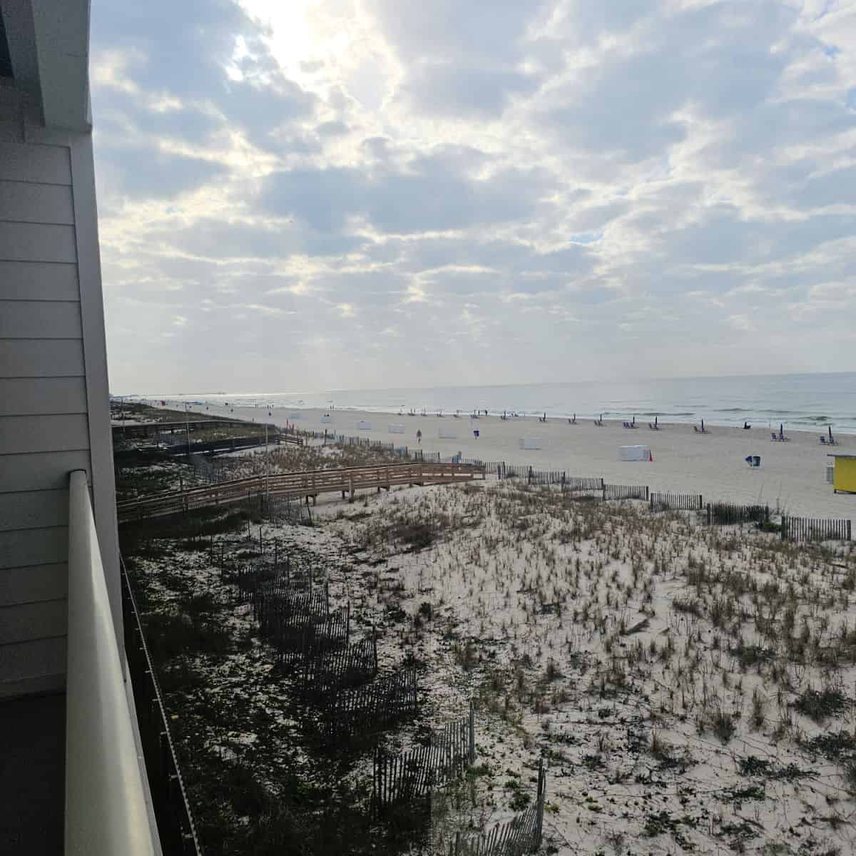 looking over a deck to the beach with walkways over the sand dunes, chairs set up along the beach, gulf water in the background.