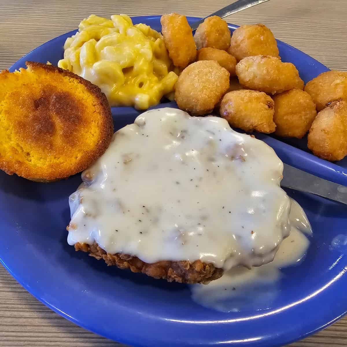Blue plate with gravy smothered meat, cornbread, mac n cheese, and corn nuggets