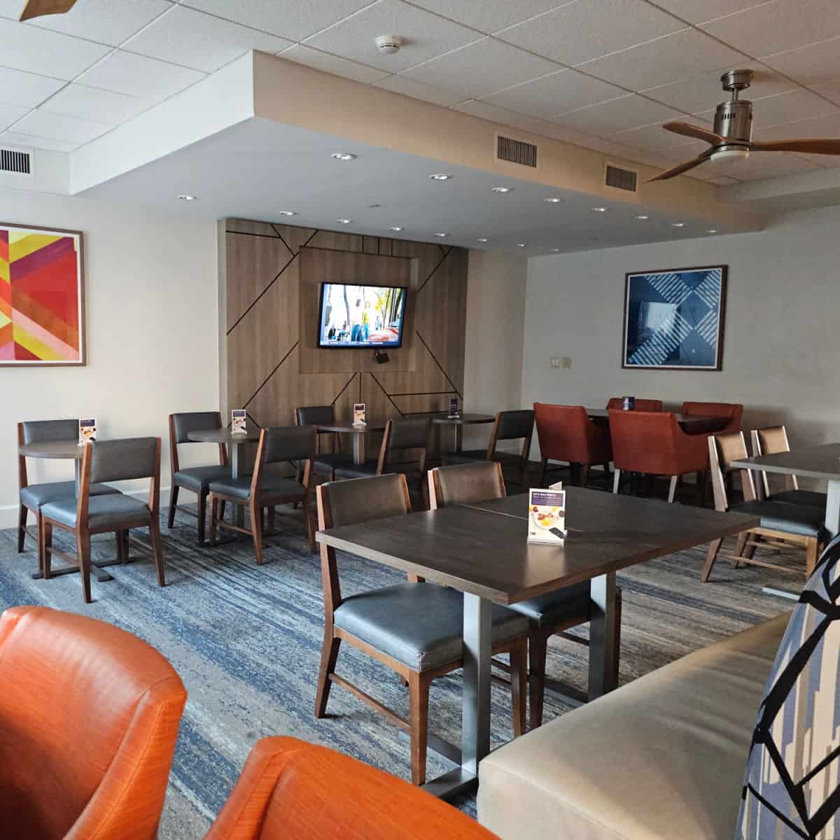 hotel breakfast area with tables and chairs, tv on the wall, art on the wall