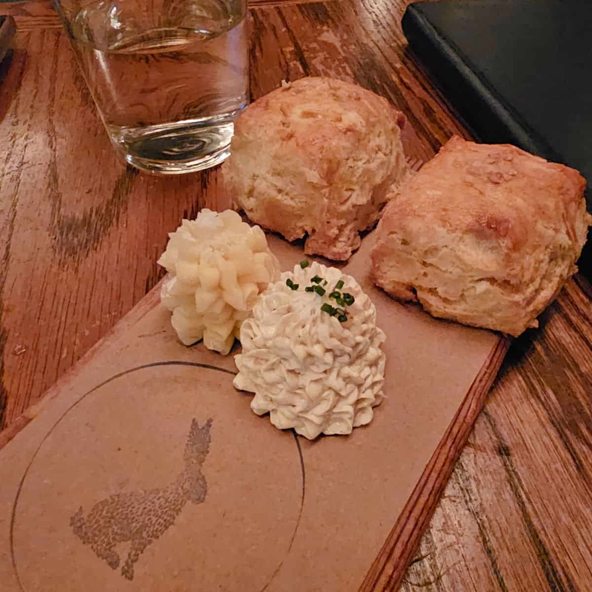 two buttermilk biscuits with 2 mounds of butter on a brown paper with a bunny stamped on it at Compere Lapin