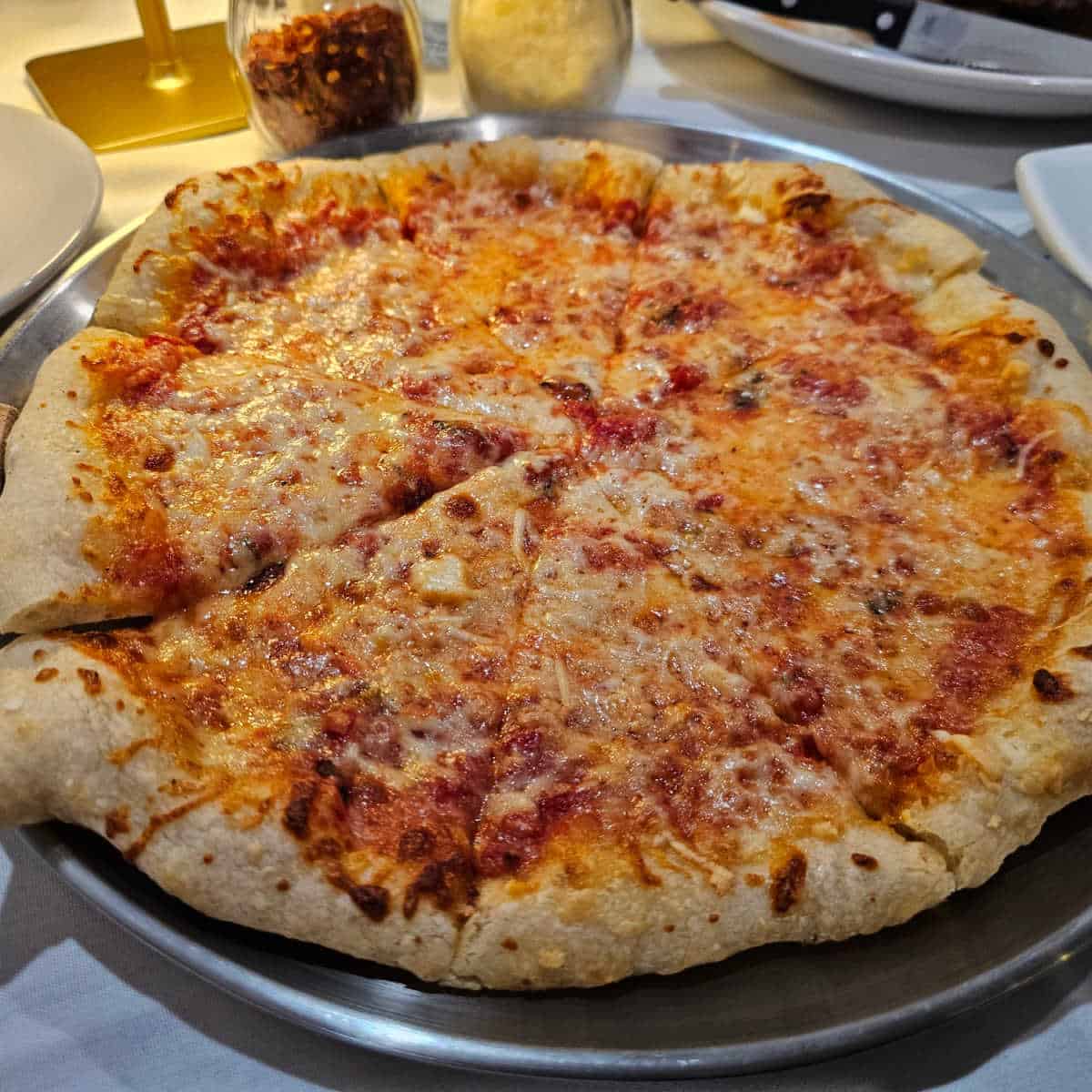 cheese pizza on a silver tray with plates behind it