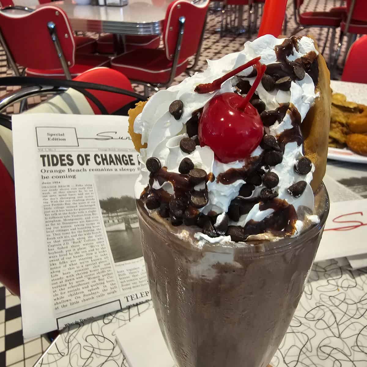 chocolate shake with whipped cream, chocolate chips, and a cherry next to the sunliner paper