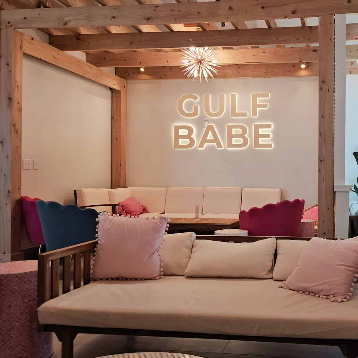 Gulf Babe sign on a wall under a wooden pergola with couches and colorful chairs