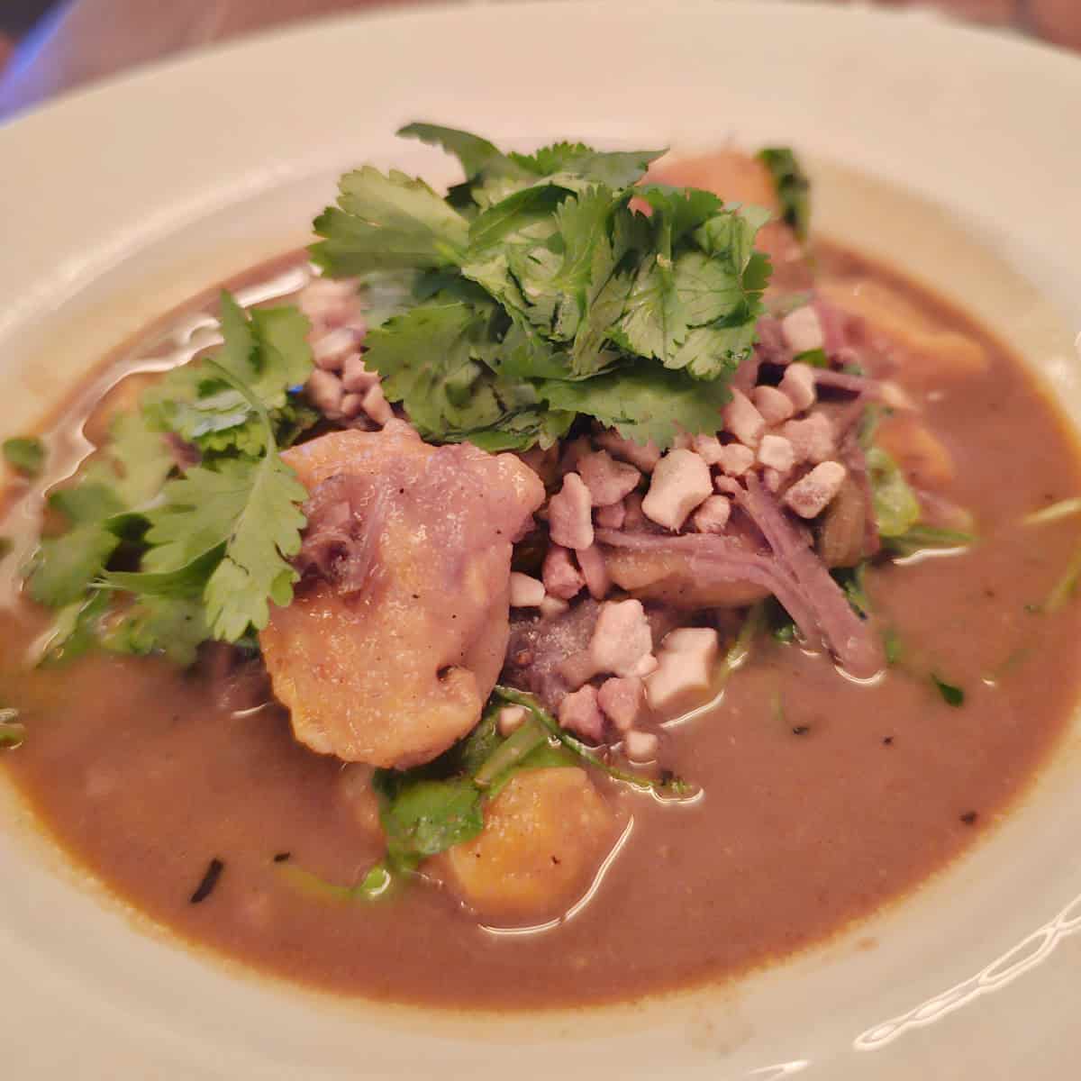 Curry Goat in a broth in a white bowl at Compare Lapin