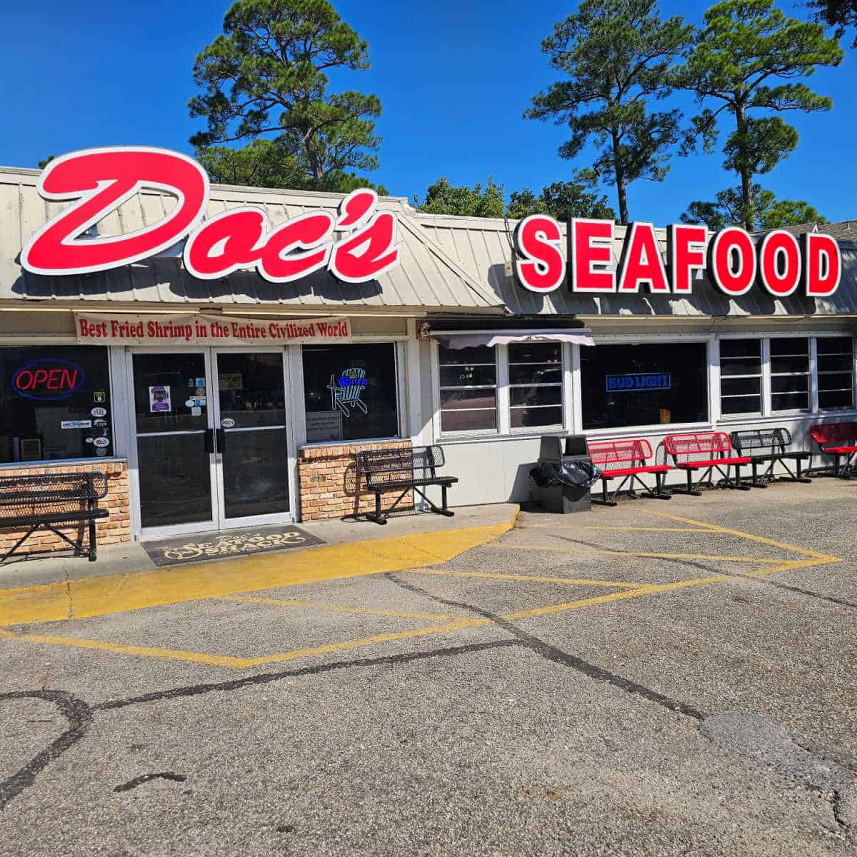 Doc's Seafood sign over the entrance to the building with a sign for the Best fried shrimp in the civilized world Black and red benches near the front entrance