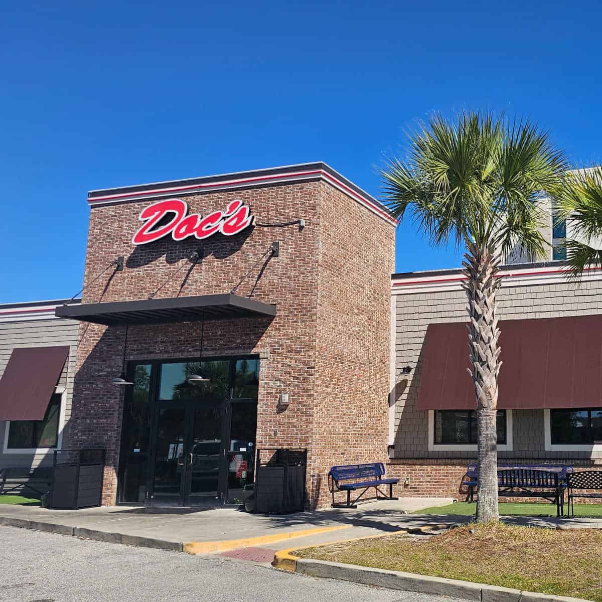 brick front on a building with Doc's on it next to a palm tree