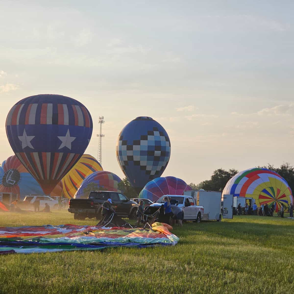 early morning mist on the grass with hot air balloons being set up and trucks in the field