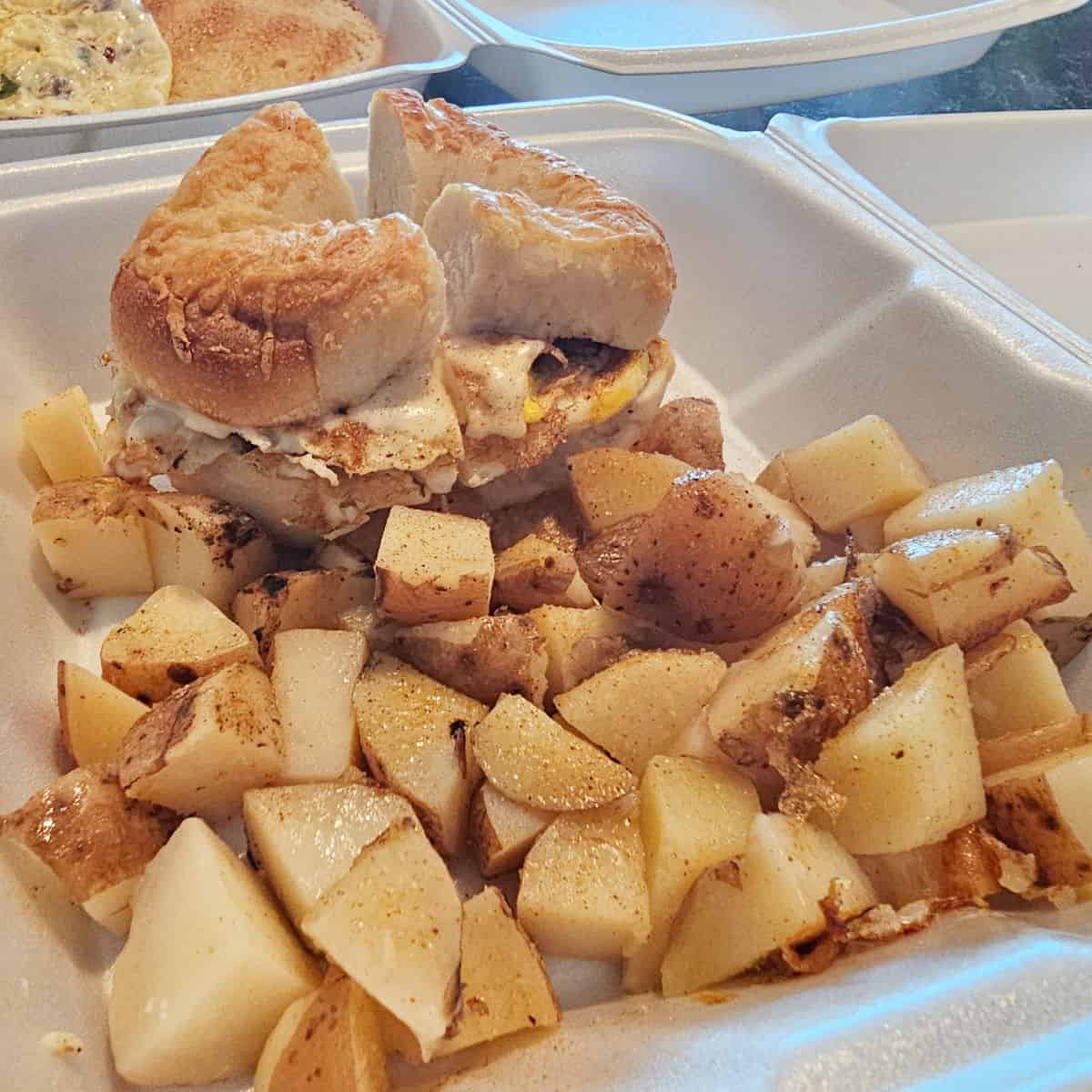 bagel breakfast sandwich in a styrofoam container with breakfast potatoes