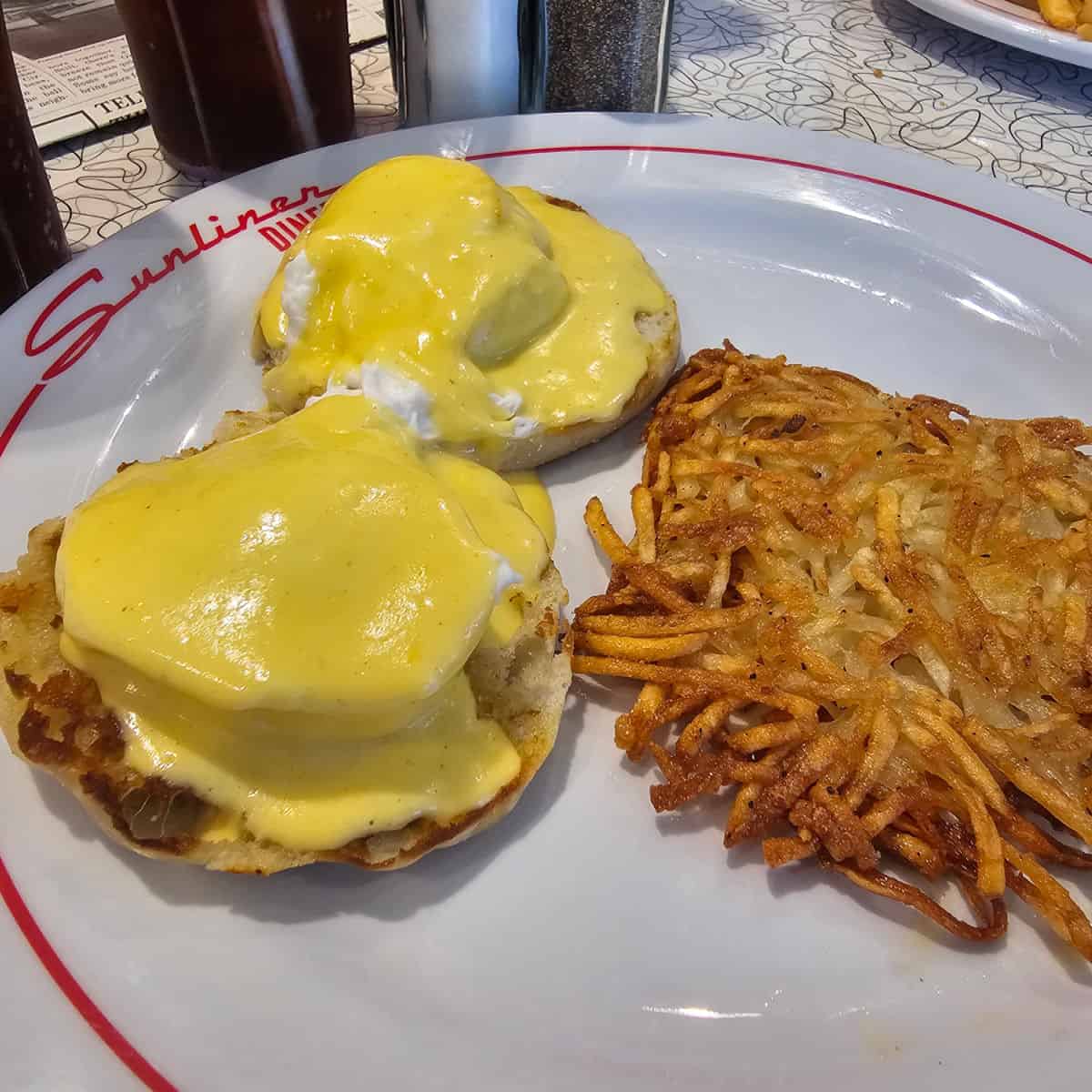 eggs benedict and hashbrowns on a white plate with sunliner diner printed on it