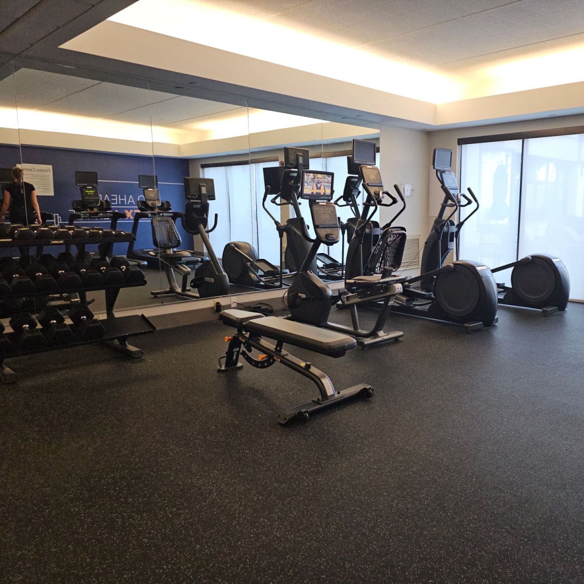 fitness center with workout bench, free weights, eliptical and mirrors.