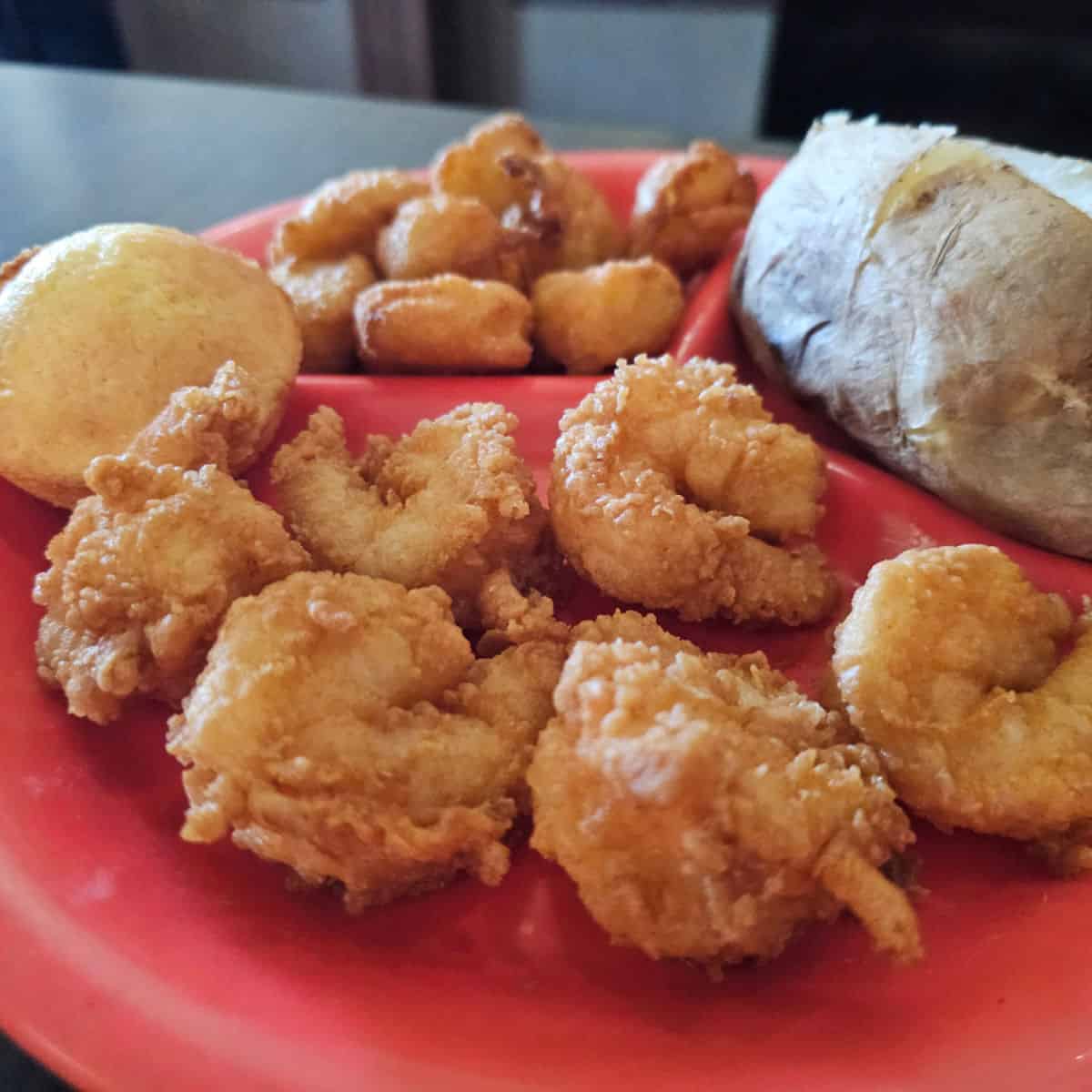 Fried shrimp with a baked potato and corn fritters on a red plate