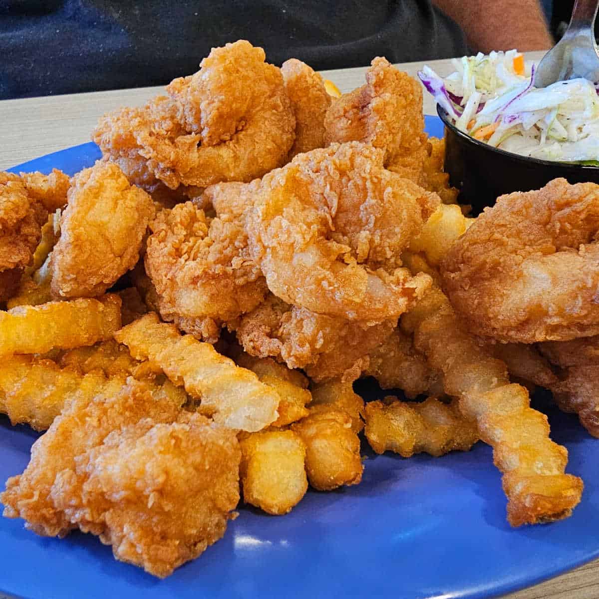 blue plate with fried shrimp and french fries next to a container of coleslaw