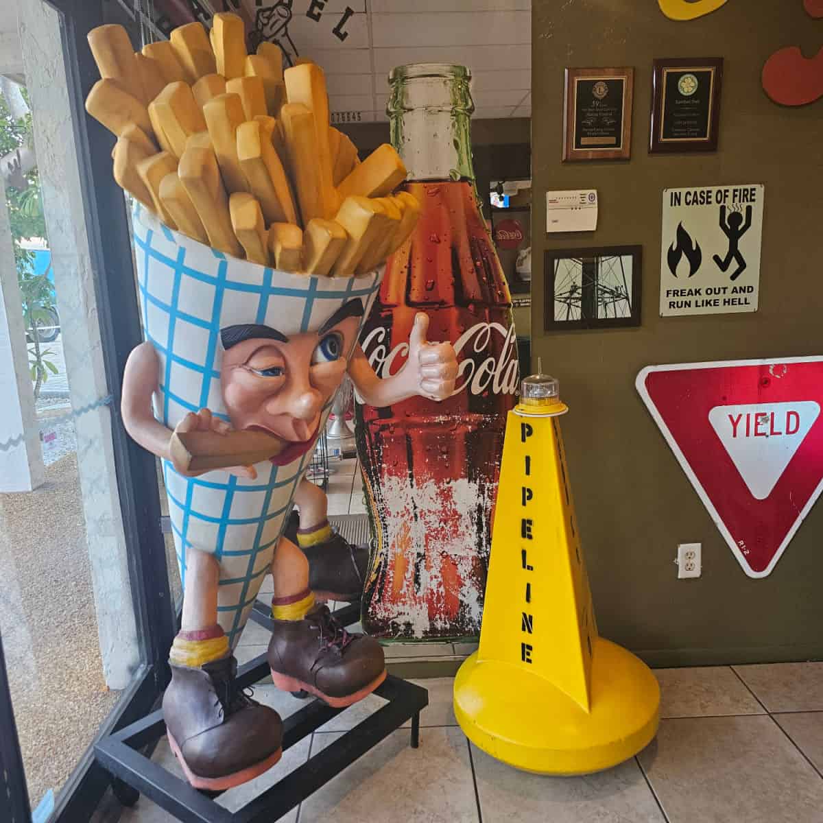 statue of a character in a frie container next to a tall cut out of a bottle of coke, next to a pipeline buoy
