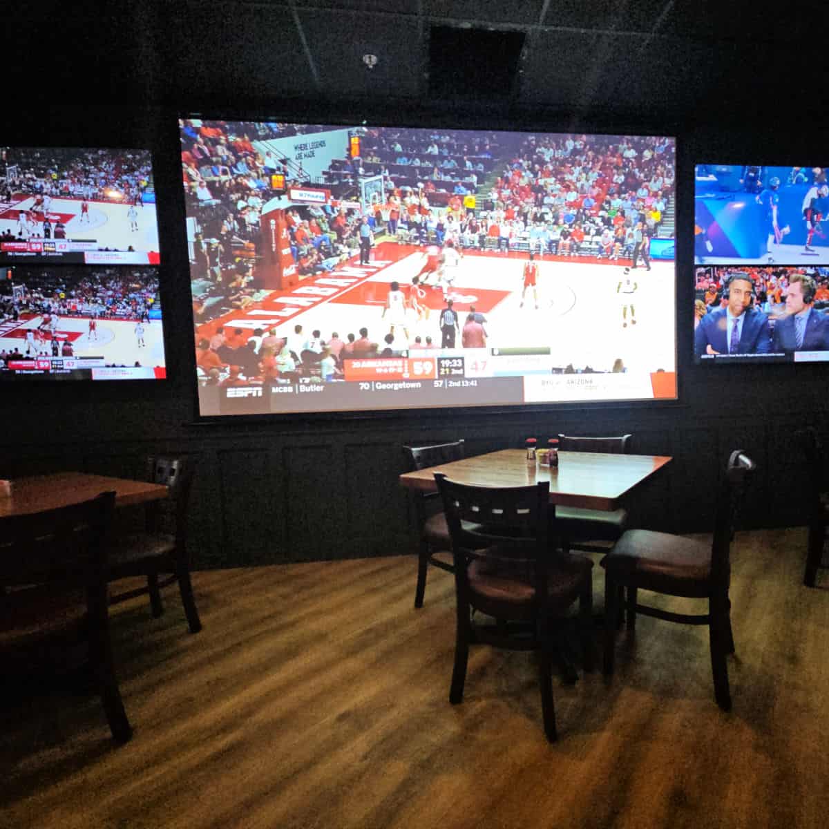 large wall of TV Screens playing sports with tables in front of them