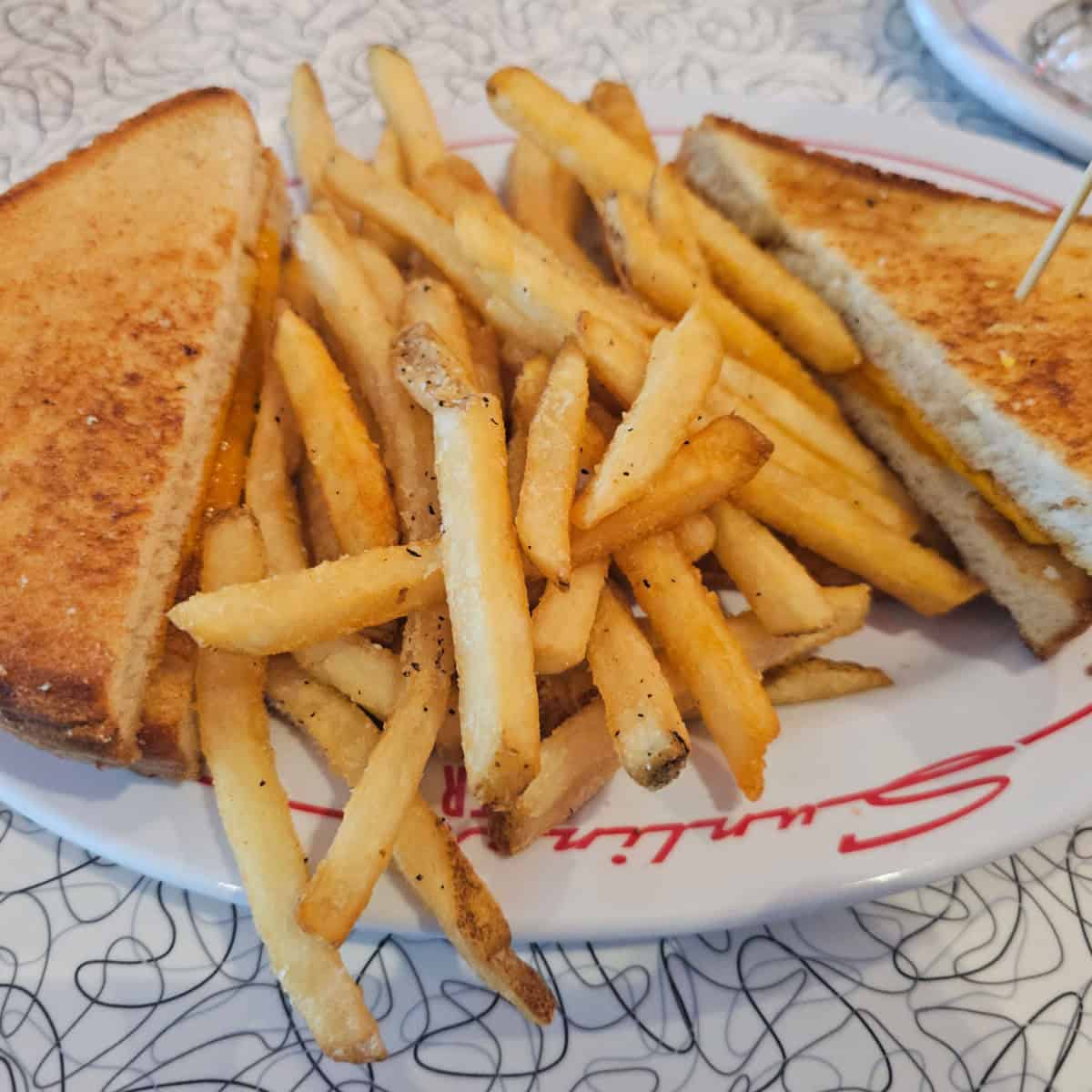 grilled cheese and fries on a white plate with sunliner printed on it