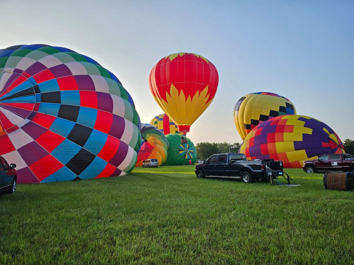 hot air balloons going up and getting set up in a grassy field with a truck in the middle of them
