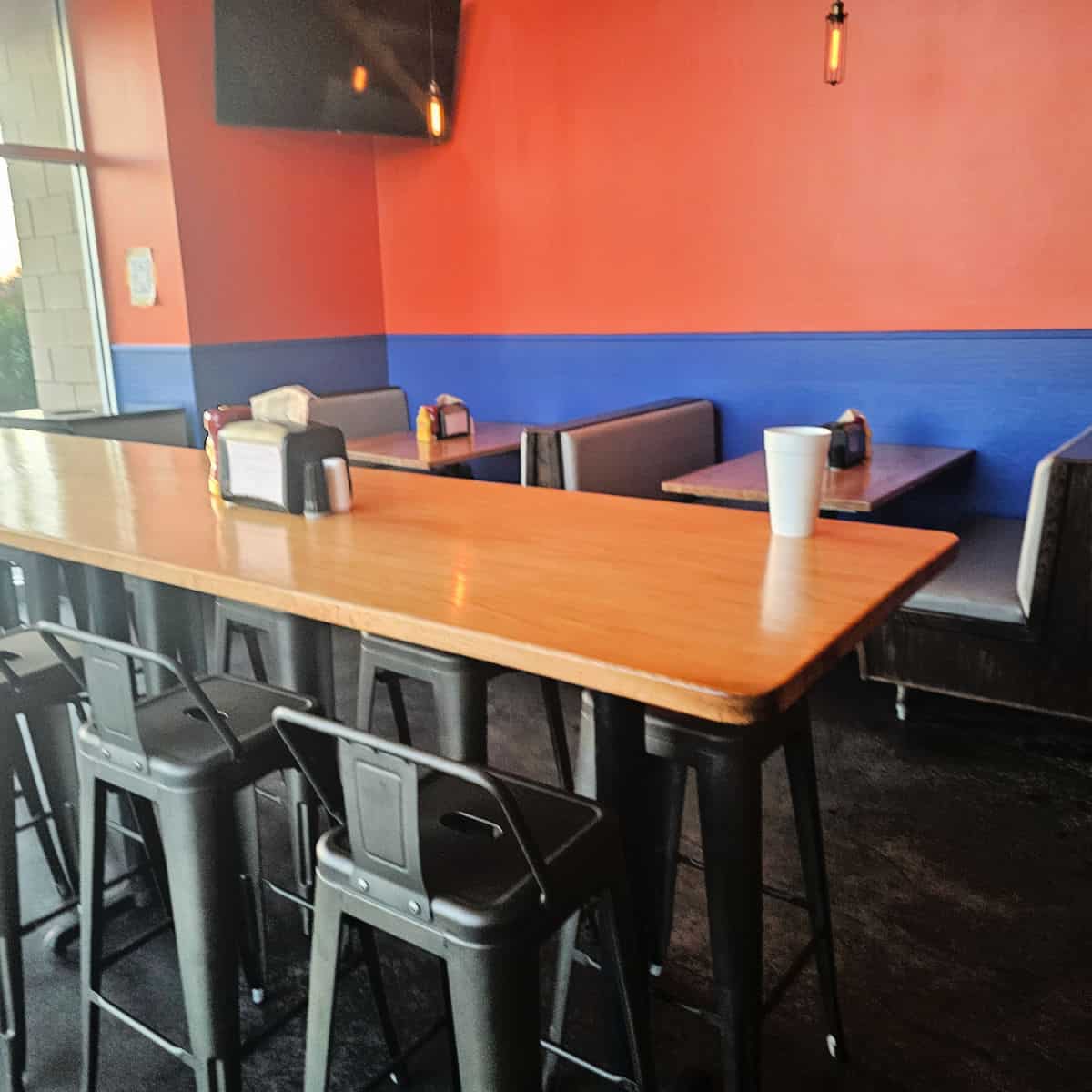 tall table with chairs near booths with padded seats, orange and blue walls