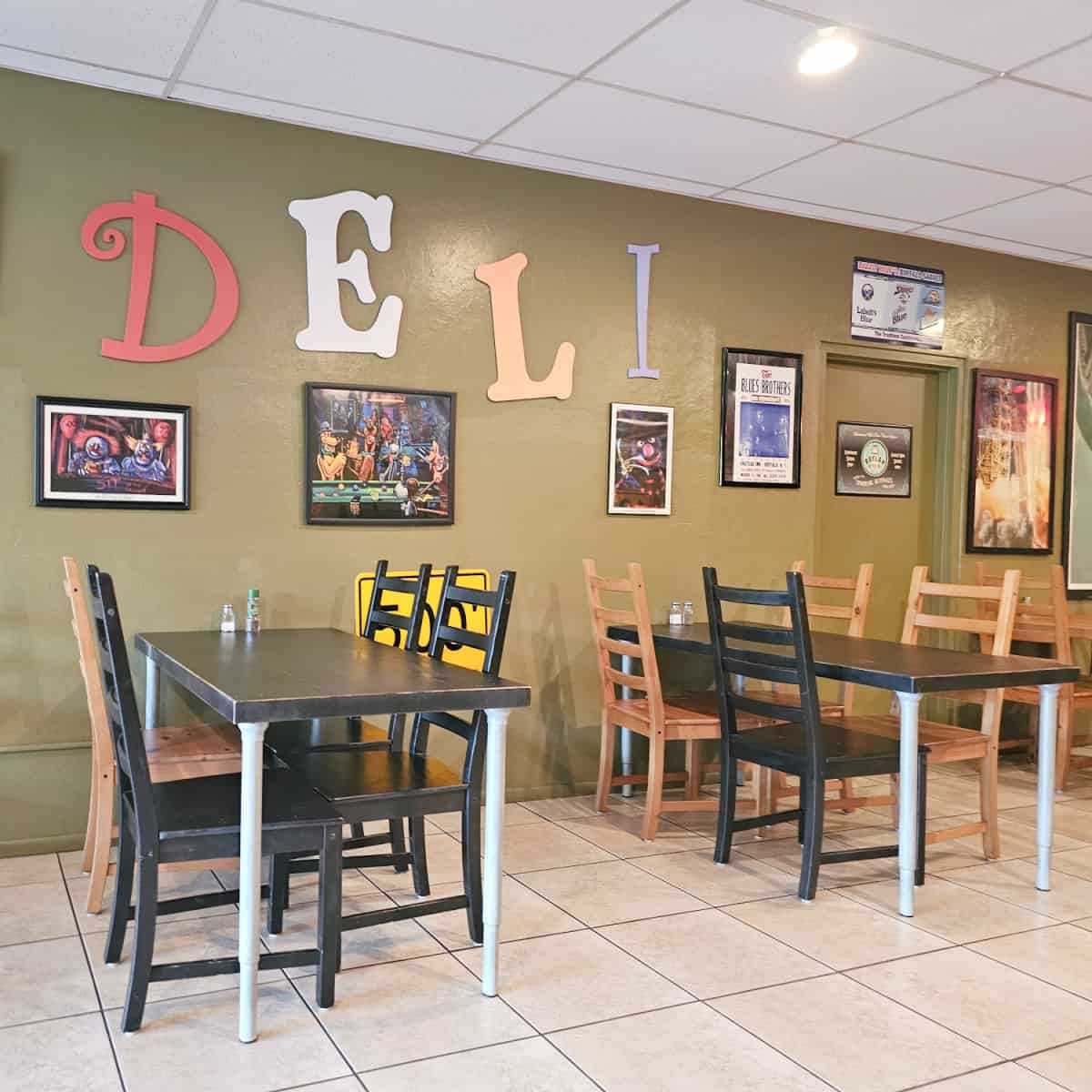 Deli written on the green painted wall with big letters, funny photos above tables with mismatched chairs