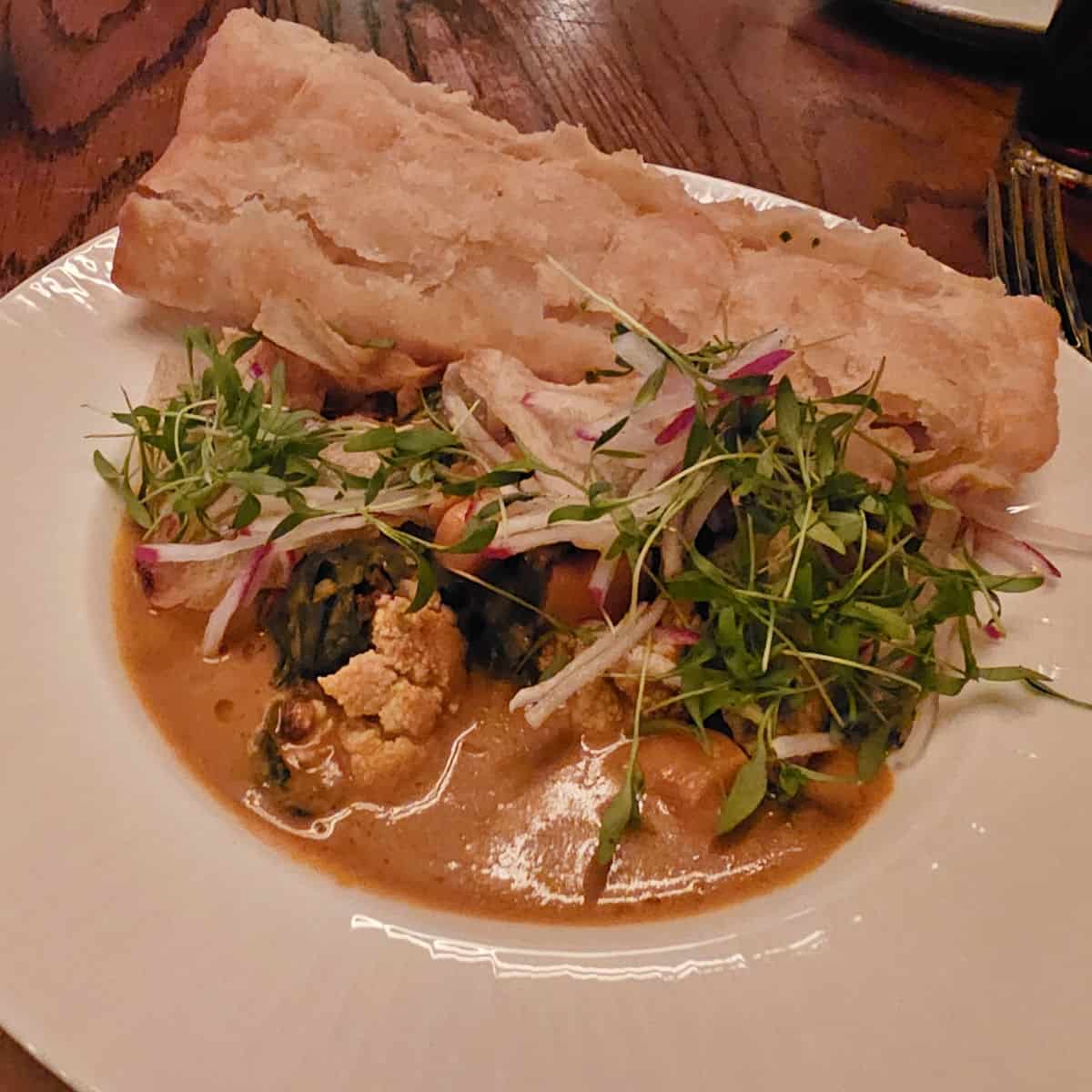 Ital Stew with Chive Roti in a white bowl with a fork next to it at Compare Lapin