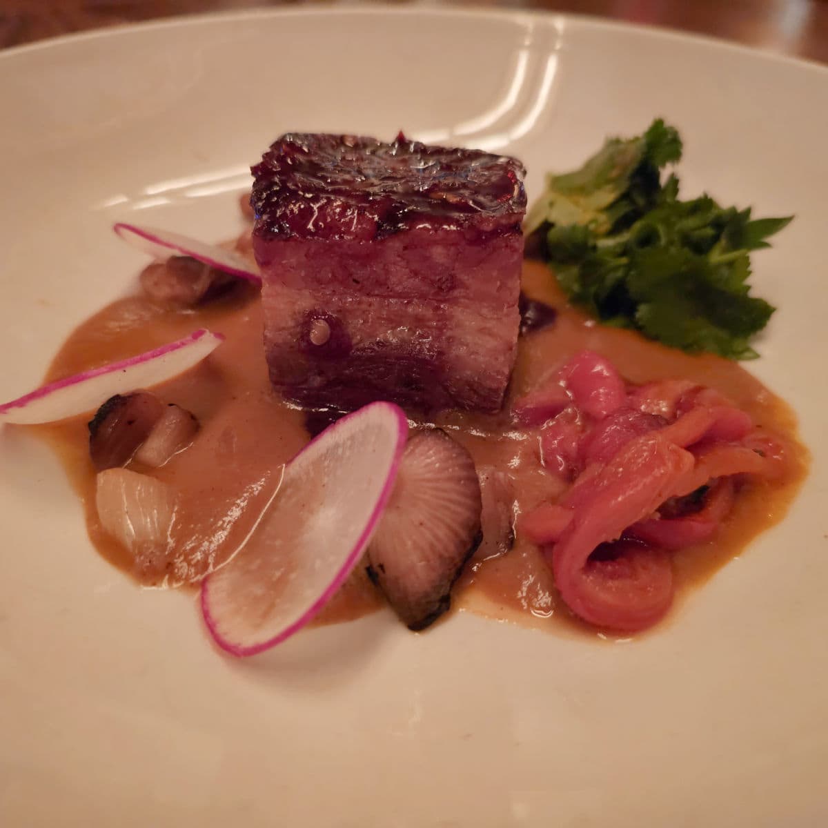 pork belly with pickled onions and radish in a white bowl