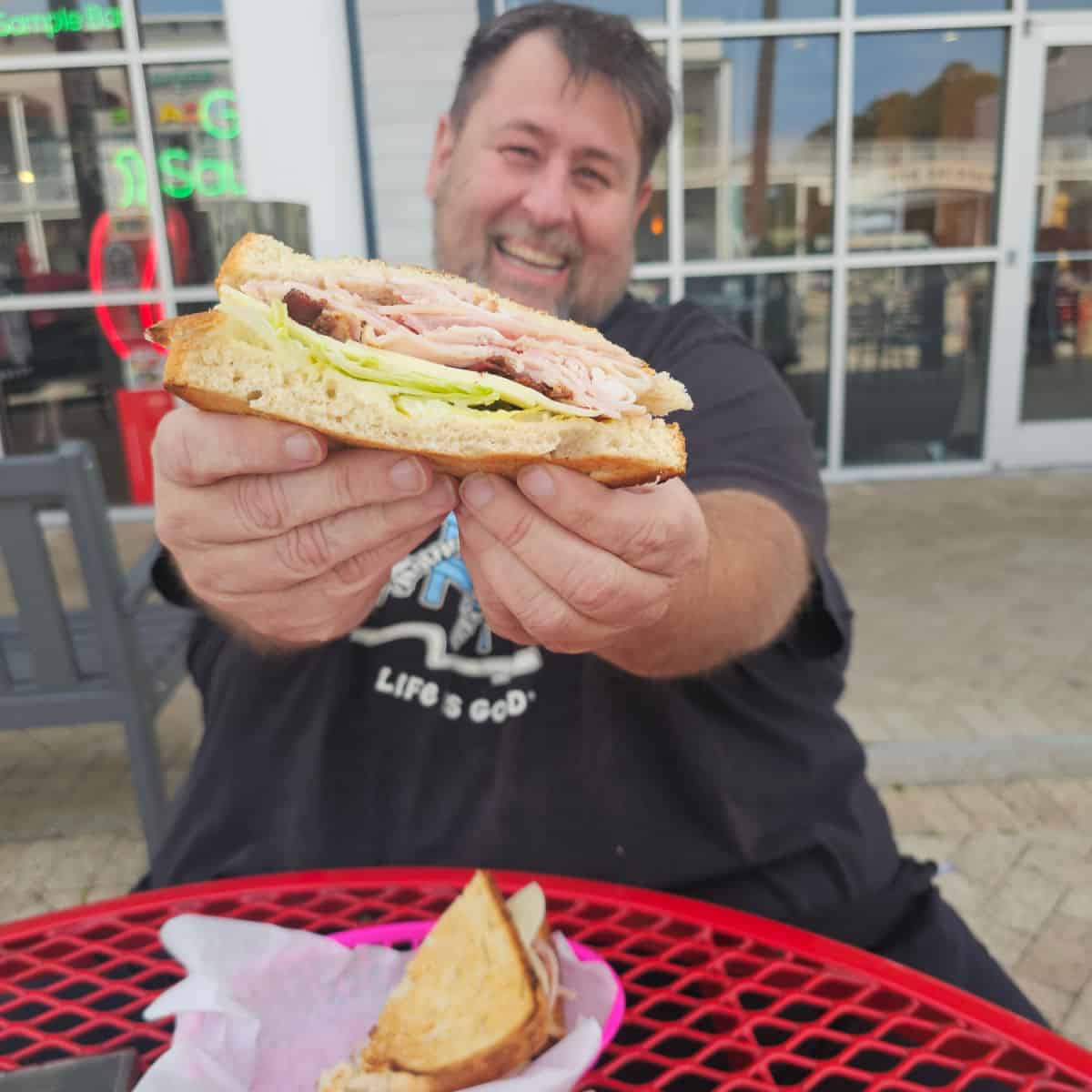 john holding his sandwich out in front of him over a red table