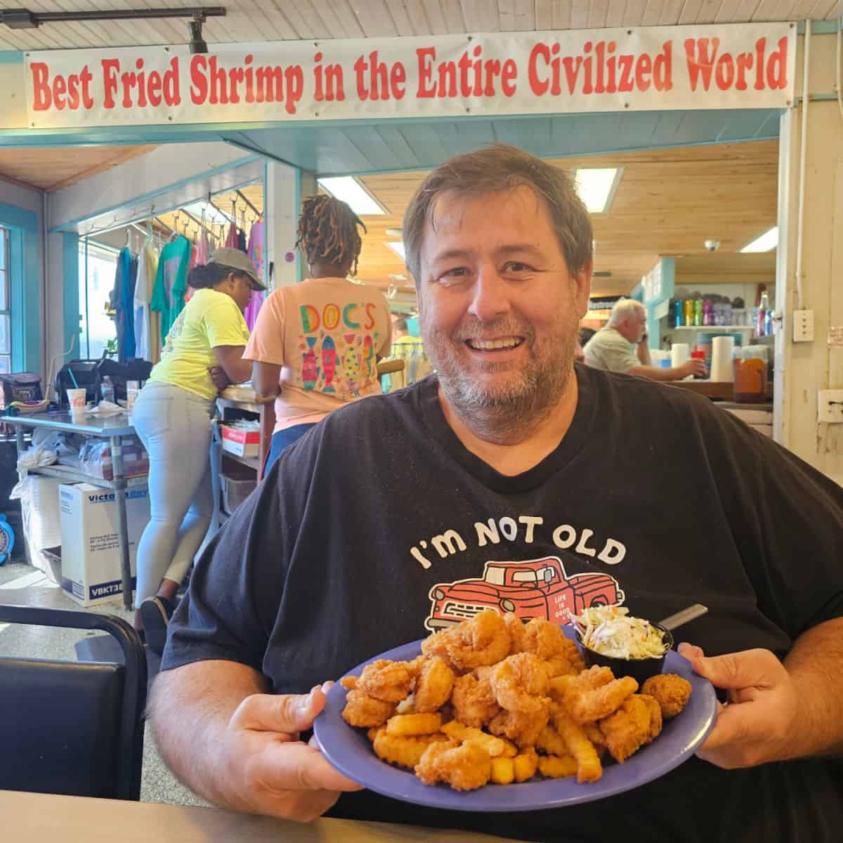 John holding a plate of fried shrimp under the Best Fried Shrimp in the Entire Civilized World sign
