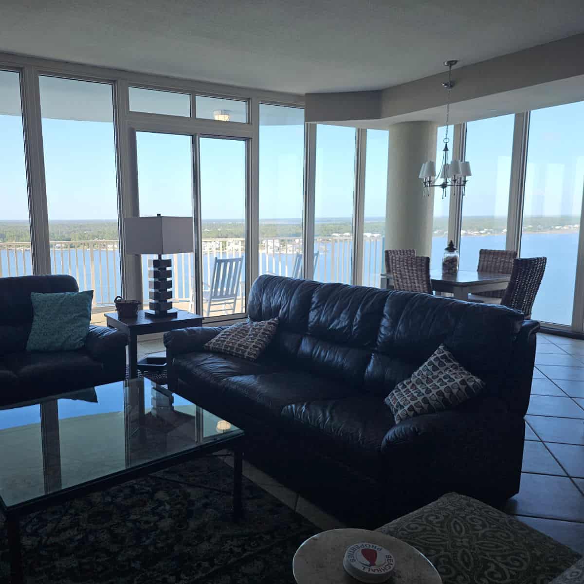 Living room with leather couches, glasstop table, Beachball Properties coasters, and large picture windows looking out to Little Lagoon from the 15th Floor