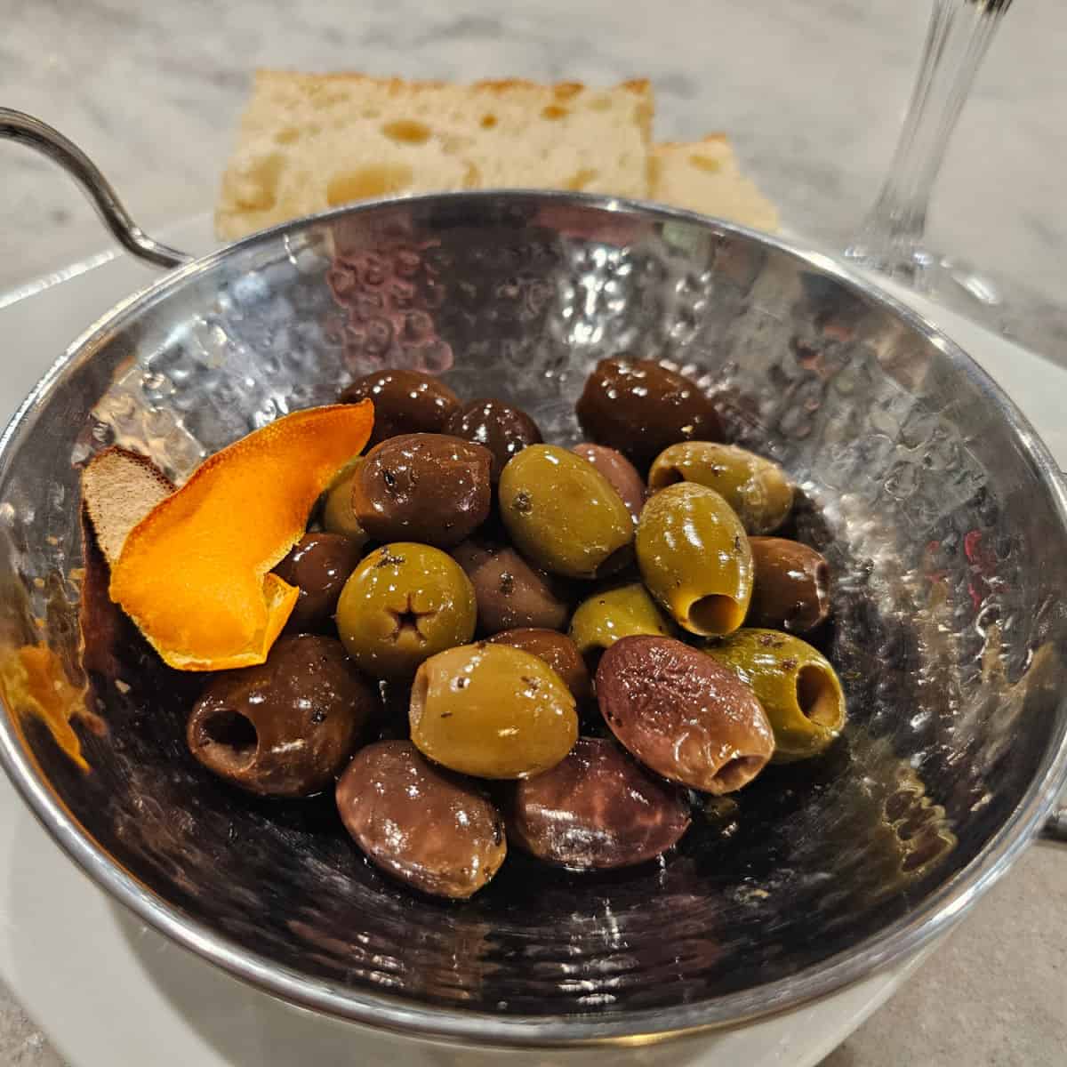 Marinated Olives in a silver bowl with bread on the side of a plate