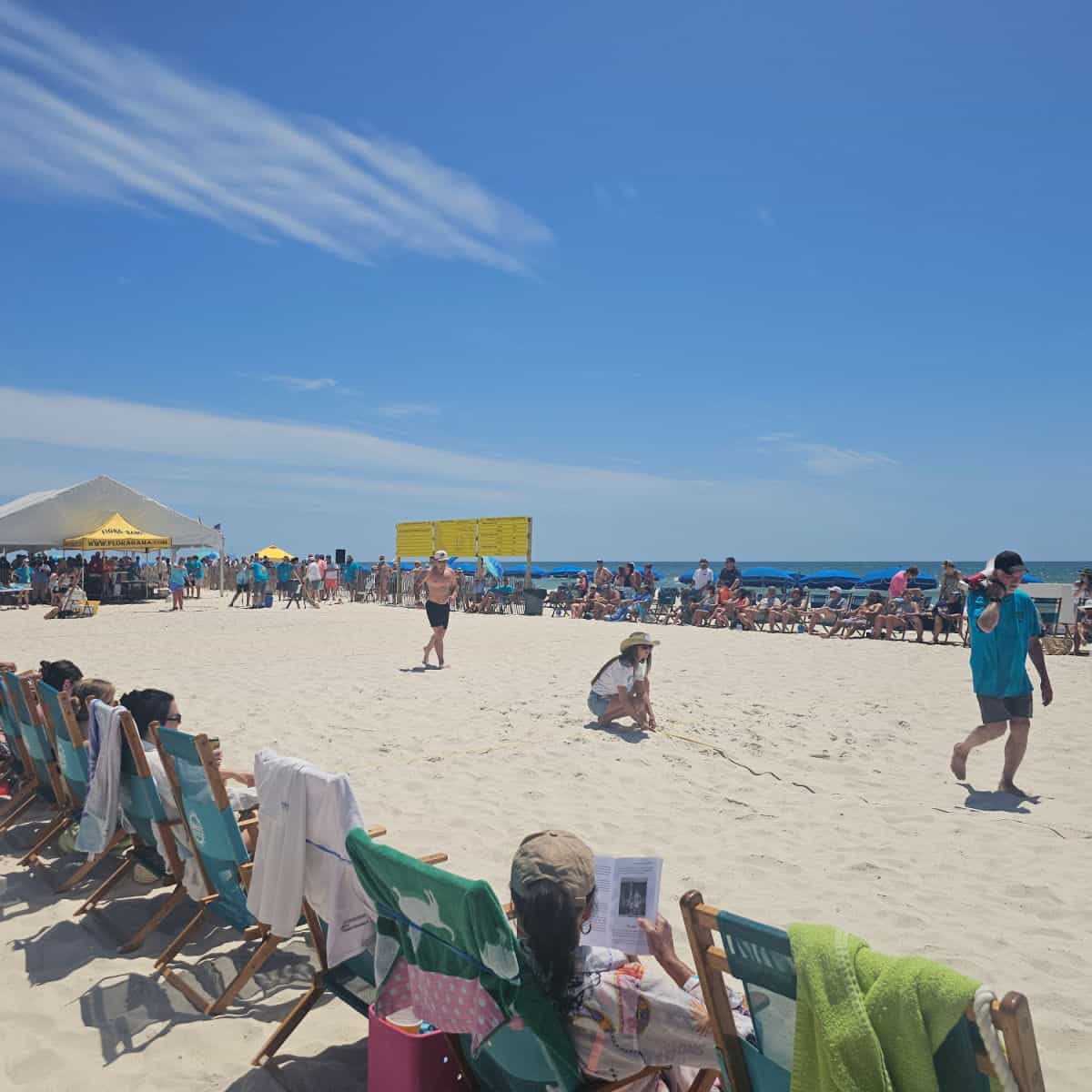 chairs lining the beach in a rectangle, flora bama tent at one end. people on the beach with a measuring tape measuring for the mullet toss